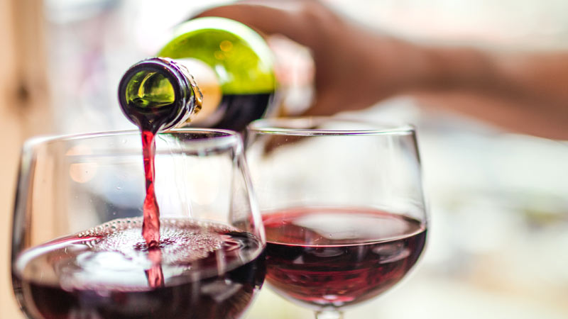 Pessoa a encher dois copos de vinho com uma garrafa de vinho tinto da casta Alicante-Bouschet.